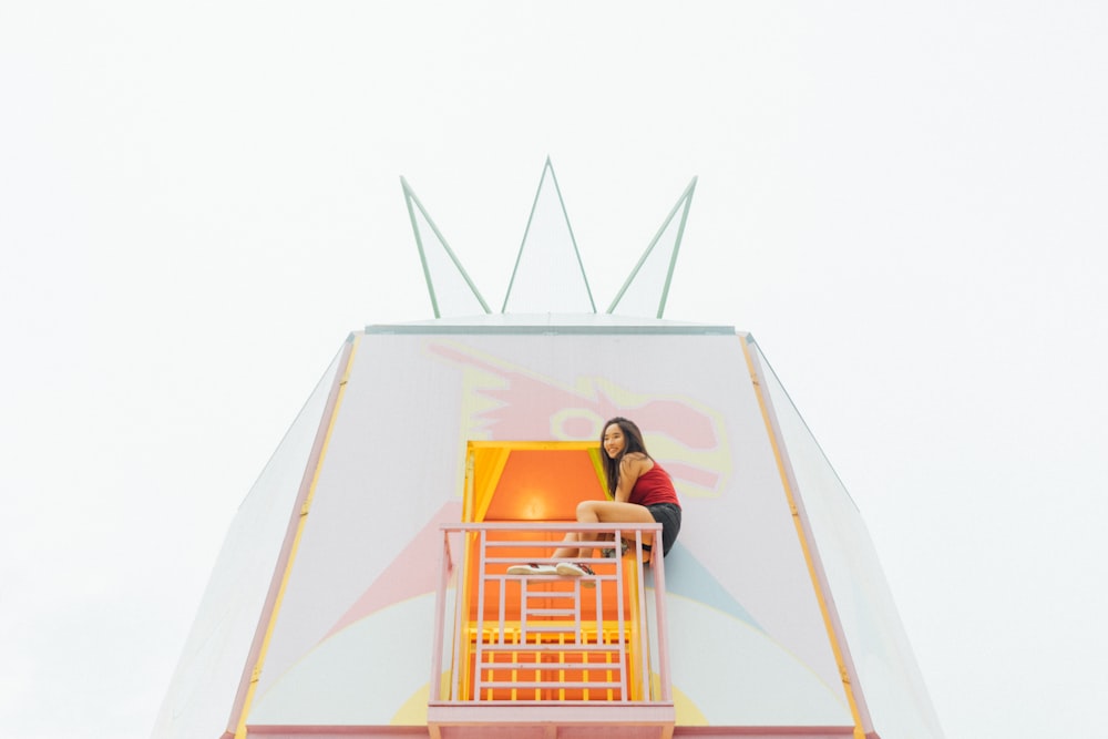 woman wearing red top sitting on pink metal rail