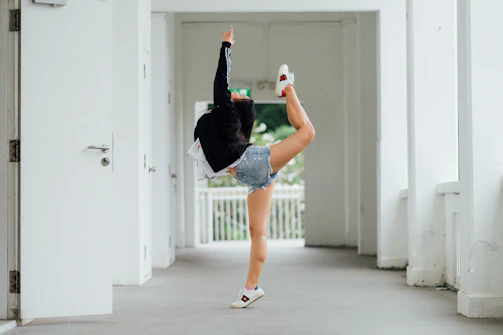 A dedicated karate student practicing a high kick in a bright dojo with green mats.