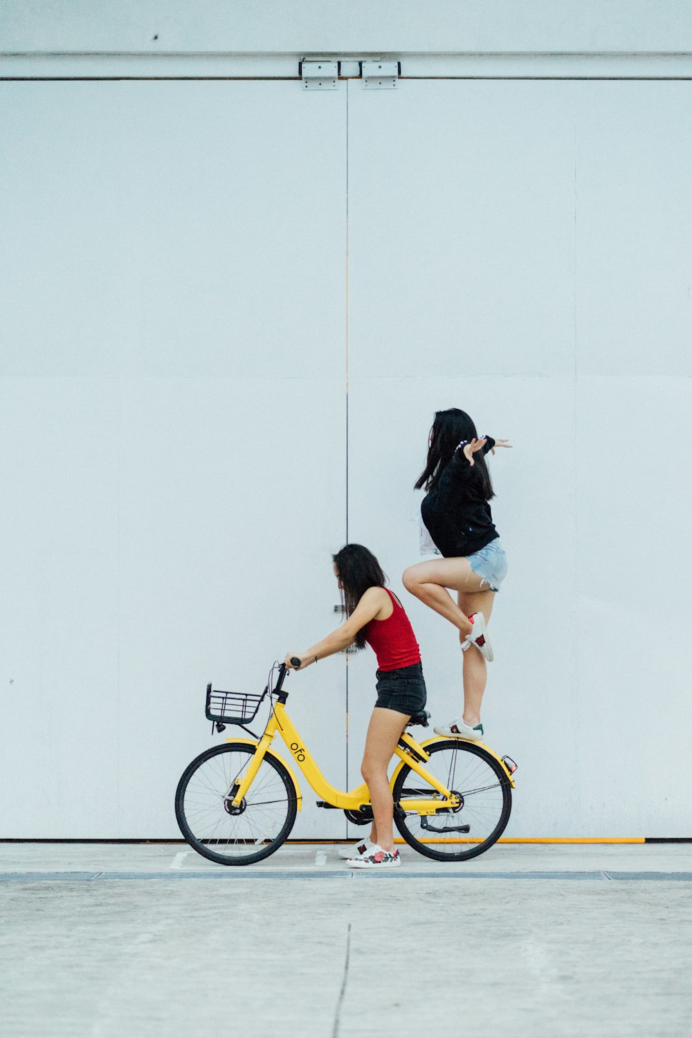 Mujer montando en bicicleta con otra mujer de pie en el guardabarros trasero cerca de la pared