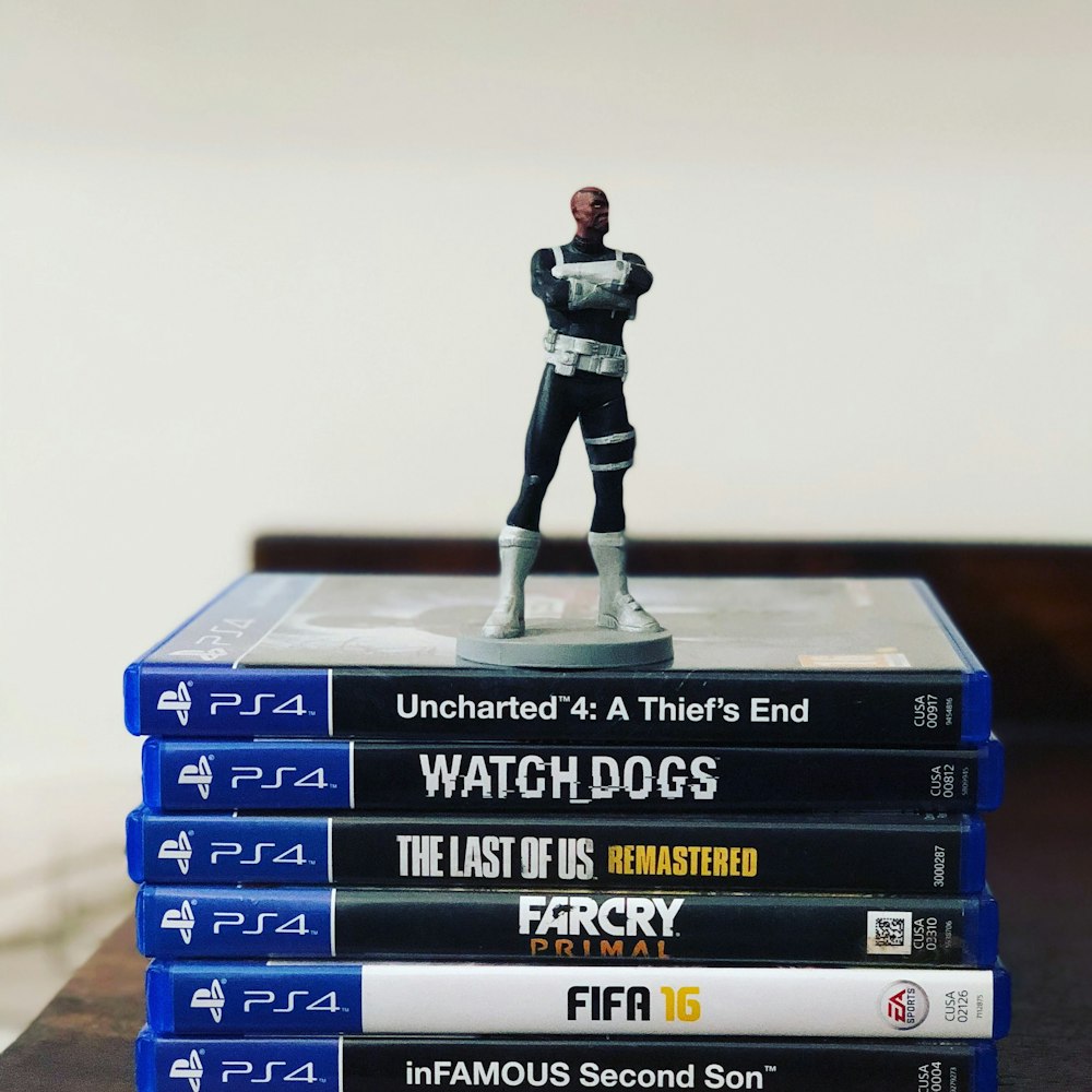assorted-title Sony PS4 game cases with figurine on top