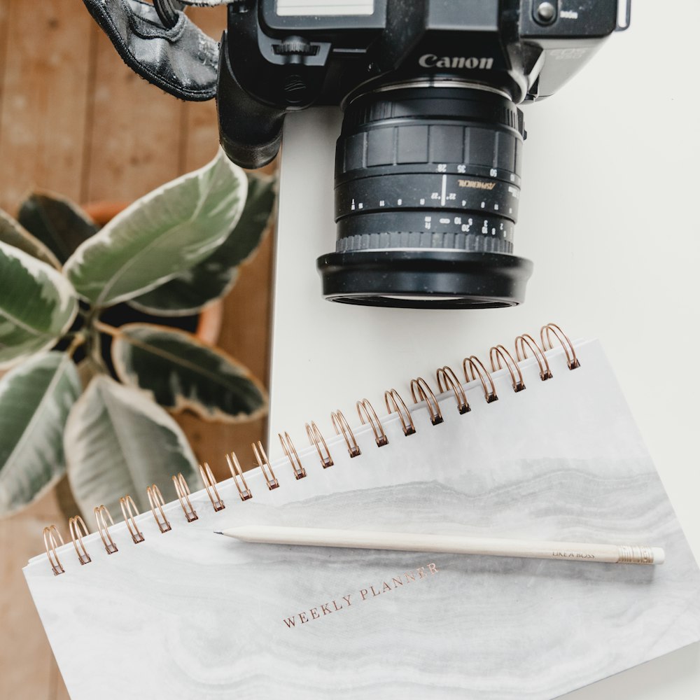 black Canon DSLR camera on table beside notebook