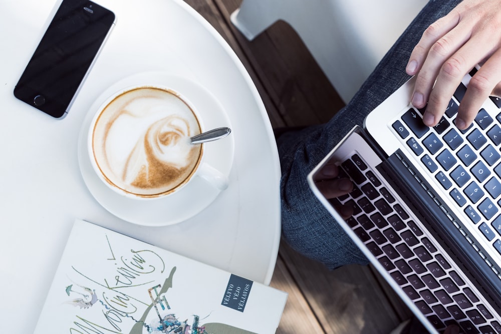 person using laptop near cup of coffee