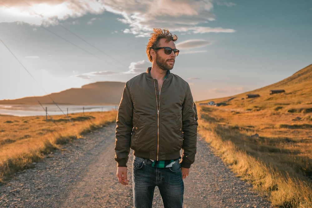 man wearing bomber jacket standing in front of pathway