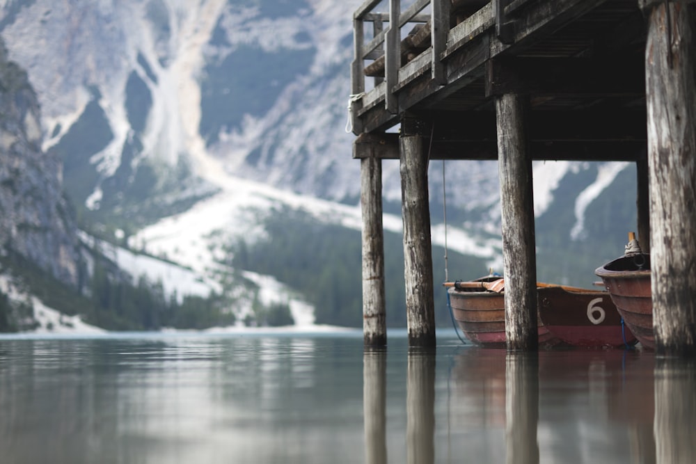 two brown wooden canoe under dock with mountain in distance