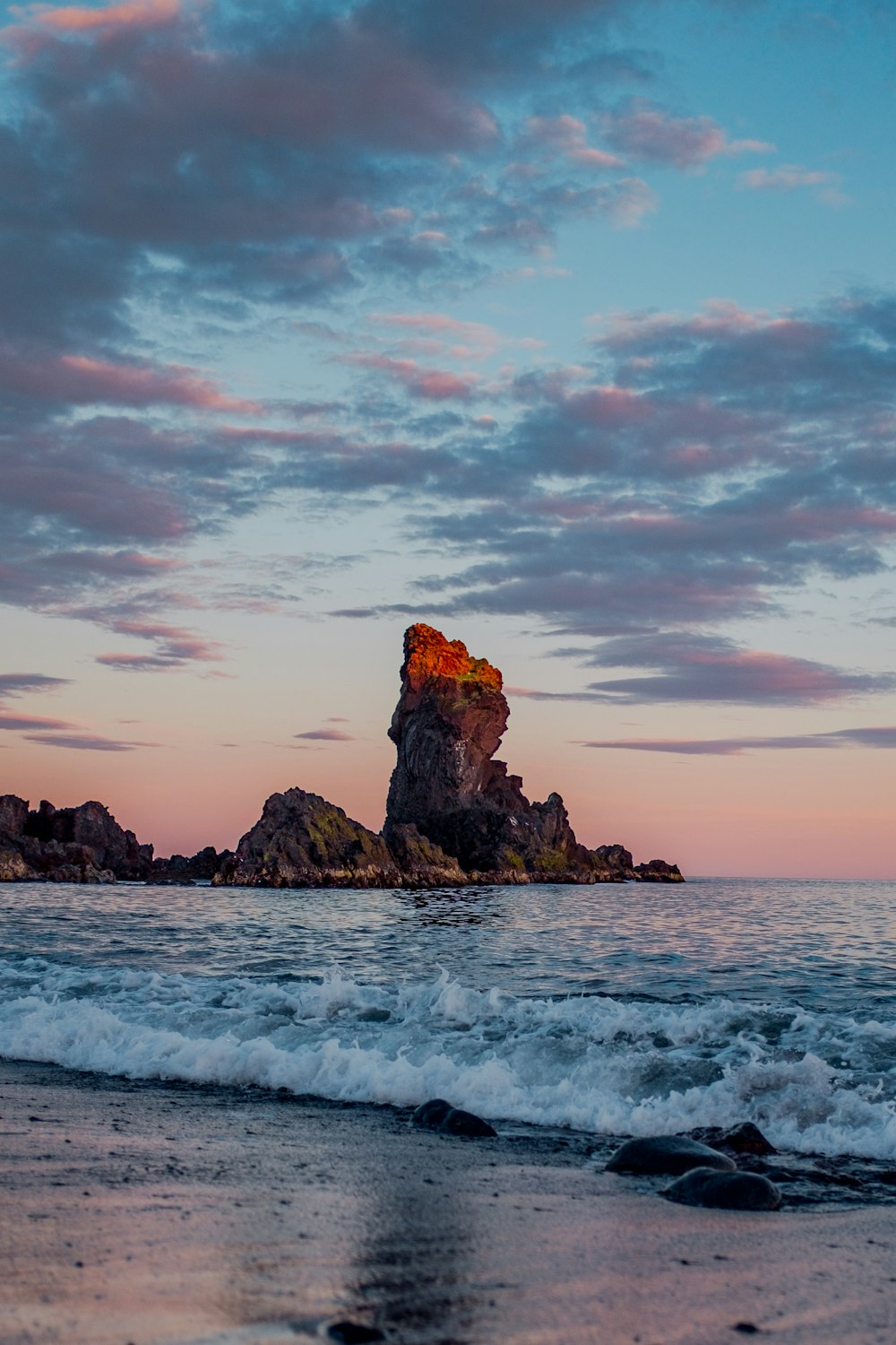 ocean waves on shore with rock formation in distance under gray clouds during daytime