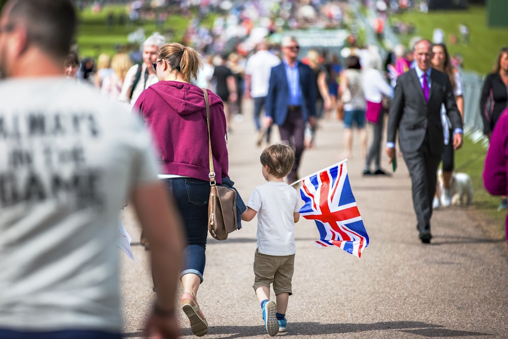 fotografía de enfoque selectivo de niño sosteniendo la bandera del Reino Unido caminando por un camino lleno de gente