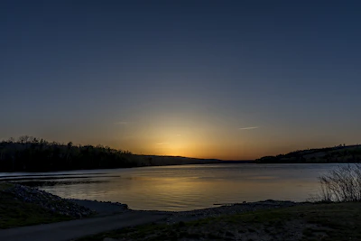 A serene landscape showing a calm lake reflecting the soft colors of a sunset.