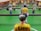 A close-up view of a foosball table game with focus on a yellow-shirted foosball figurine in the foreground. The figurine has the name 'Eddy' written on its back. Other figurines in green and white shirts are visible in the background, lined up on metal rods. The table has a bright green surface with white markings.
