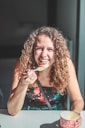woman smiling holding spoon and cup while sitting beside table