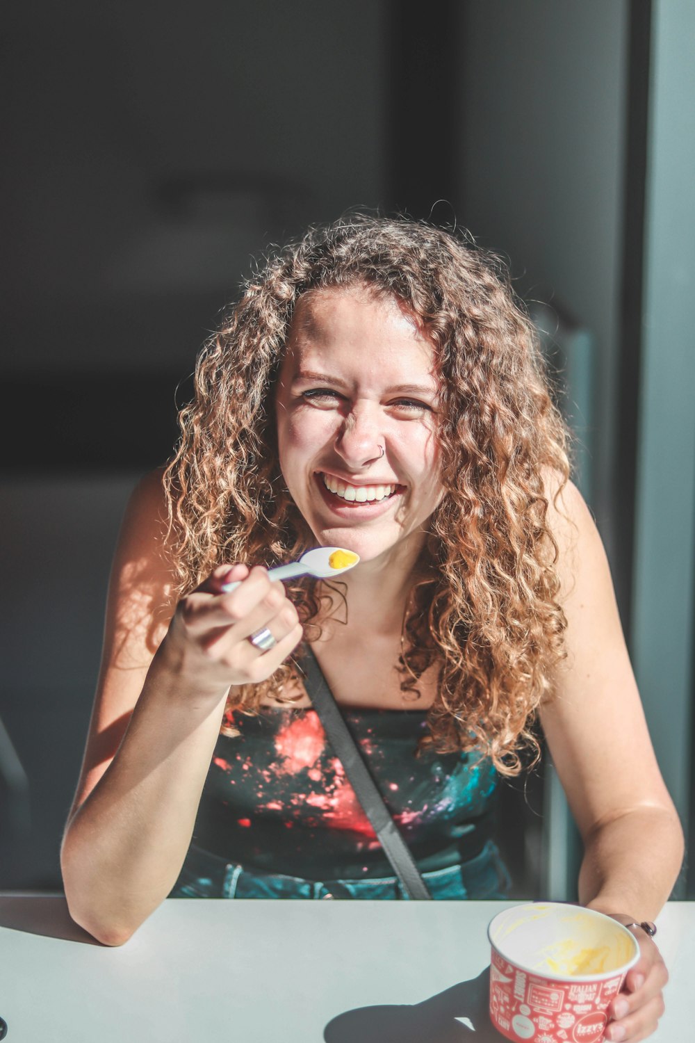 woman smiling holding spoon and cup while sitting beside table