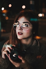 woman wearing silver-colored Aviator-style sunglasses holding camera bokeh photography