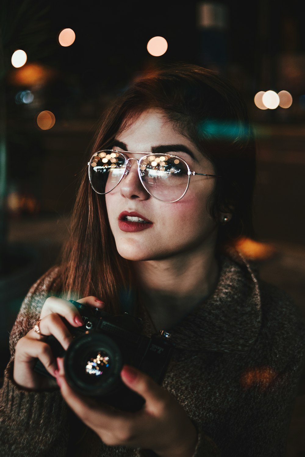 Frau mit silberfarbener Sonnenbrille im Aviator-Stil hält Kamera Bokeh Fotografie