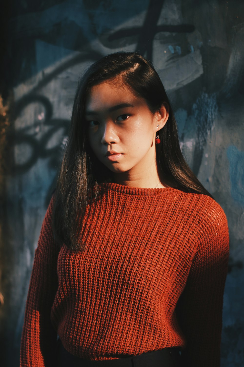 woman in red sweater posing near gray wall