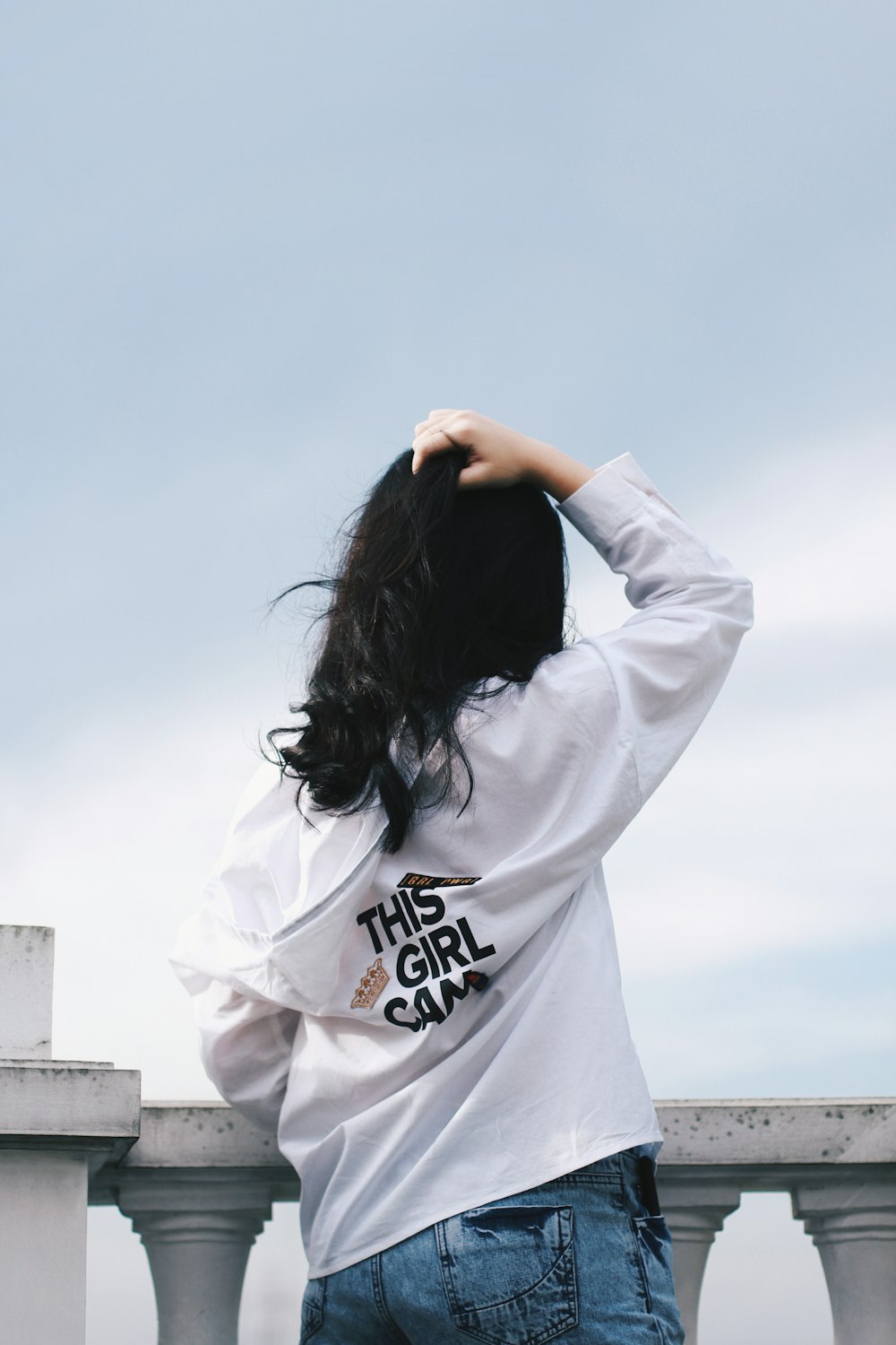 woman in front white concrete fence under gray sky