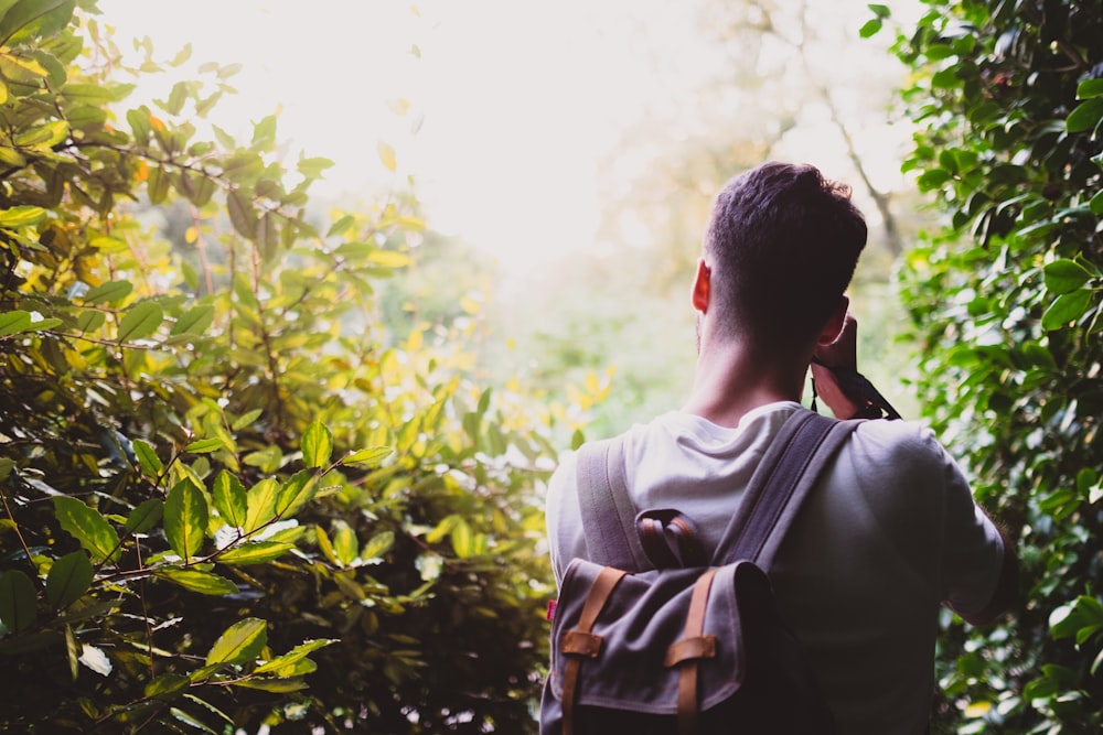 homem carregando mochila cinza entre planta de folhas verdes