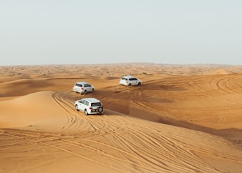 three white vehicles moving in desert under gray sky