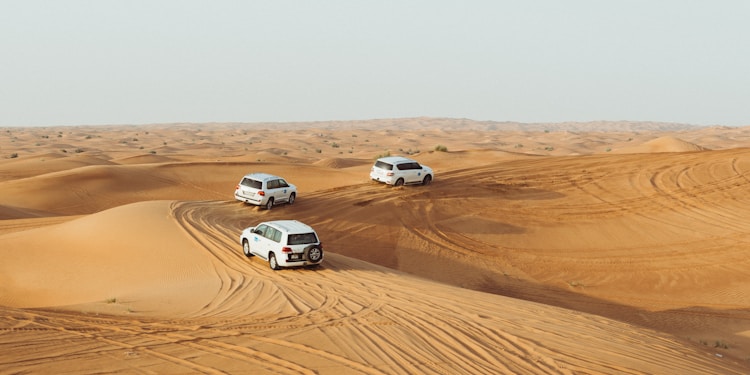 three white vehicles moving in desert under gray sky