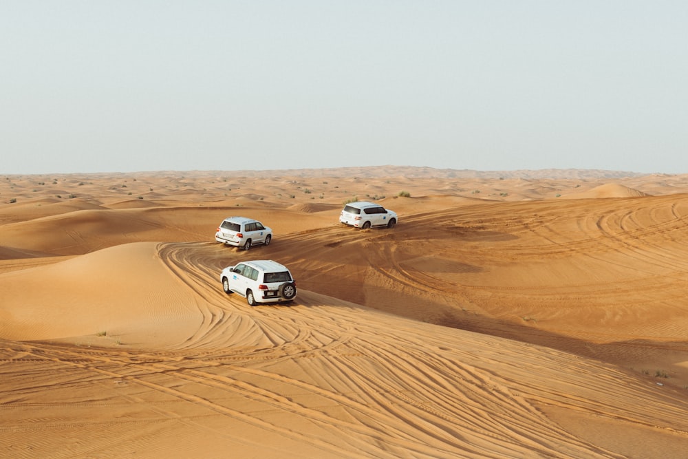 tres vehículos blancos moviéndose en el desierto bajo un cielo gris