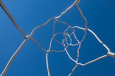 A twisted metal wire sculpture ascends towards a clear, deep blue sky, creating a sense of upward movement and complexity.