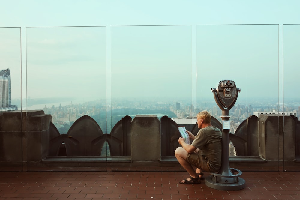 man sitting alone while reading paper on coin-operated telescope
