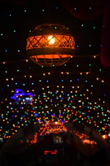Warm glowing lanterns hanging above a rustic wooden bed framed by stone walls.