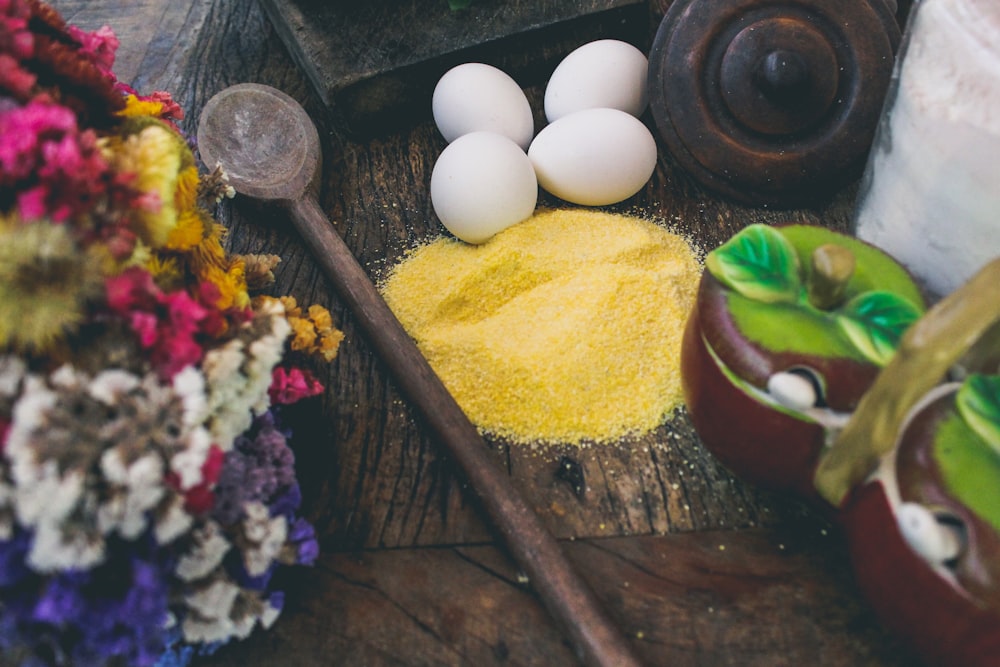 four white eggs beside yellow granules on brown wooden surface