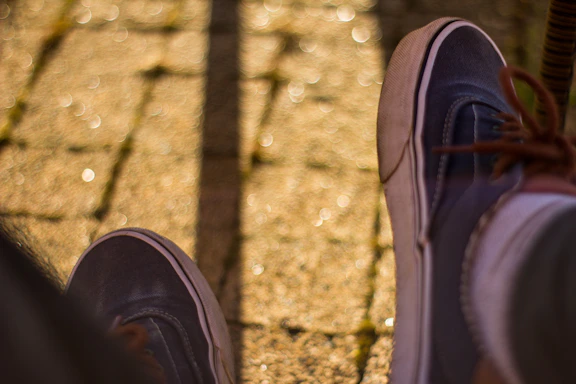 Close-up of a child's feet wearing stylish sneakers, walking on a sunny sidewalk.