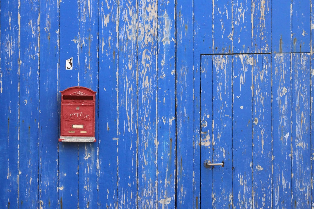 Buzón de metal rojo sobre pared de madera azul