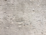 A textured concrete wall with noticeable wear and small holes throughout the surface. There are visible grooves and lines, likely from the construction process.