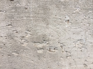 A textured concrete wall with noticeable wear and small holes throughout the surface. There are visible grooves and lines, likely from the construction process.