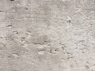 A textured concrete wall with noticeable wear and small holes throughout the surface. There are visible grooves and lines, likely from the construction process.
