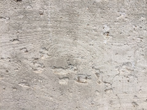 A textured concrete wall with noticeable wear and small holes throughout the surface. There are visible grooves and lines, likely from the construction process.