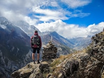 man standing on top of mountain beside cairn stones