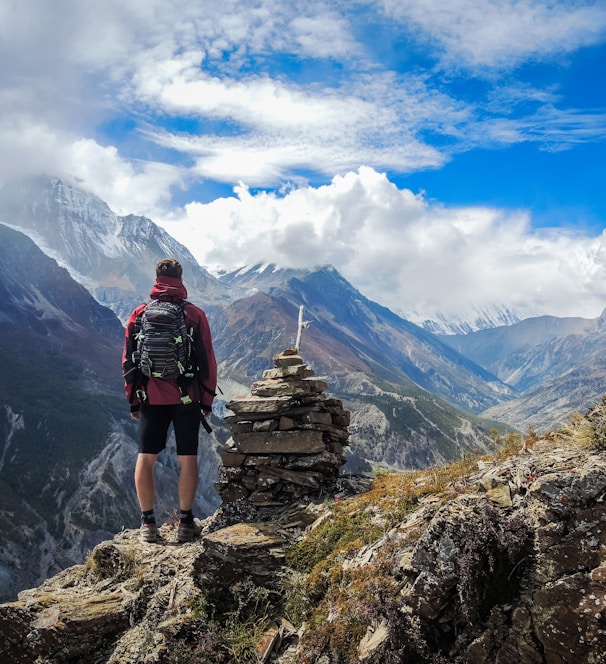 man standing on top of mountain beside cairn stones