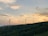 A scenic view of wind turbines on a green hillside during sunset.