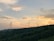 A scenic view of wind turbines on a green hillside during sunset.
