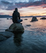 man sitting on rock surrounded by water