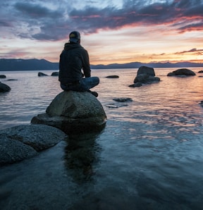 man sitting on rock surrounded by water