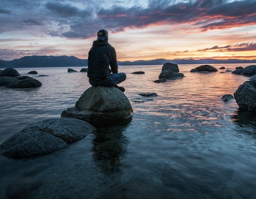 man sitting on rock surrounded by water