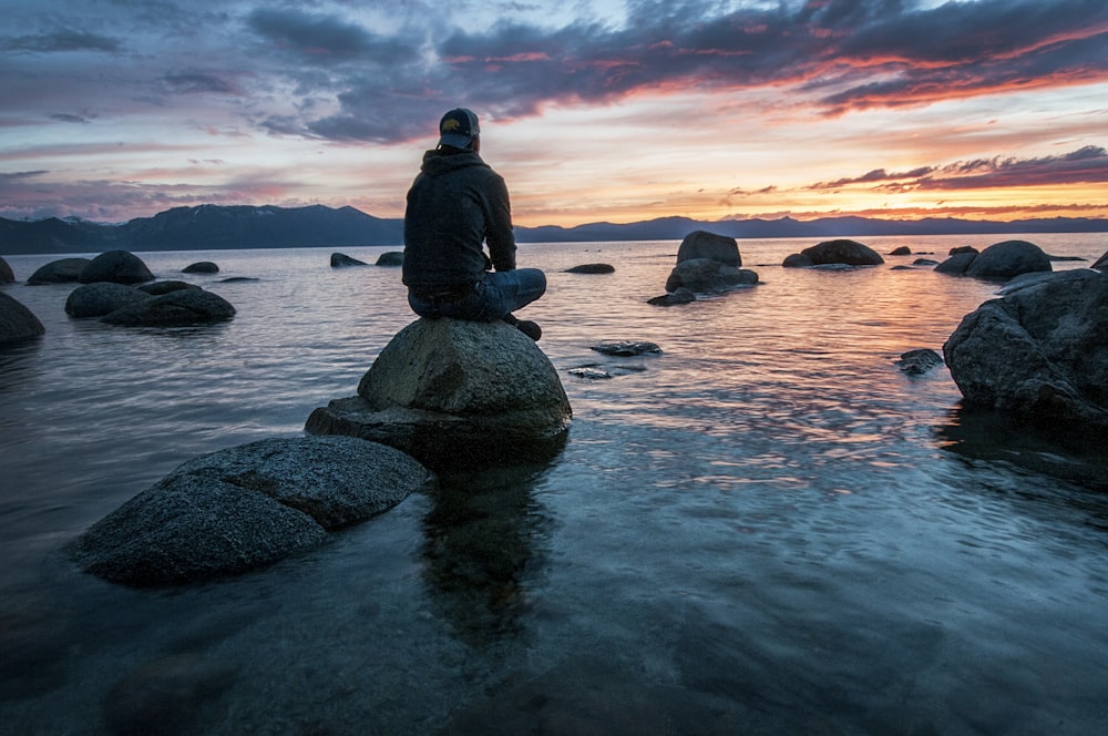 Mann sitzt auf Felsen, umgeben von Wasser