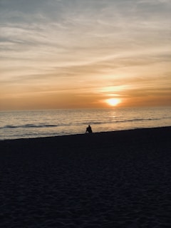 A serene beach sunset with a lone traveler sitting on the sand, laptop beside them, embodying the digital nomad lifestyle.