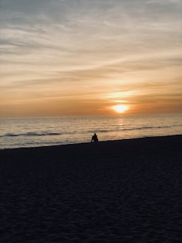 A serene beach sunset with a lone traveler sitting on the sand, laptop beside them, embodying the digital nomad lifestyle.