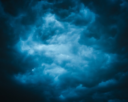 Dark clouds form a dense, swirling pattern in the sky, suggesting the onset of a storm. The texture is dramatic and turbulent, with shades of blue and gray blending together.