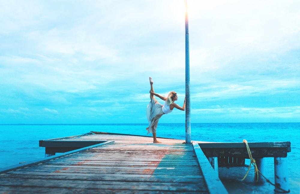 woman stretching on wooden dock while holding post by the sea during daytime