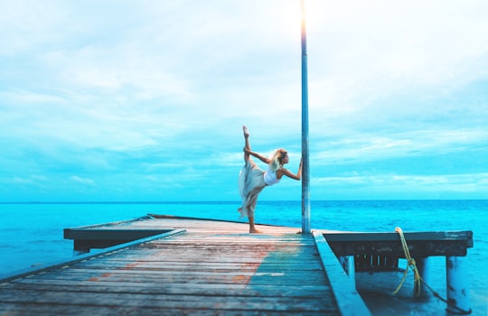 woman stretching on wooden dock while holding post by the sea during daytime in Fulidhoo Maldives