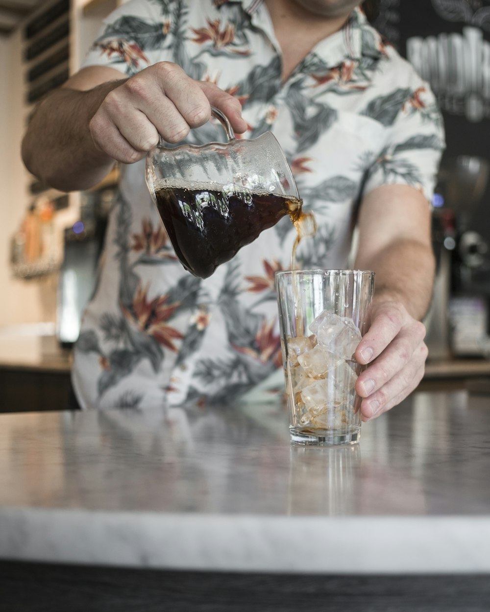 person pouring brown liquid on clear drinking glass