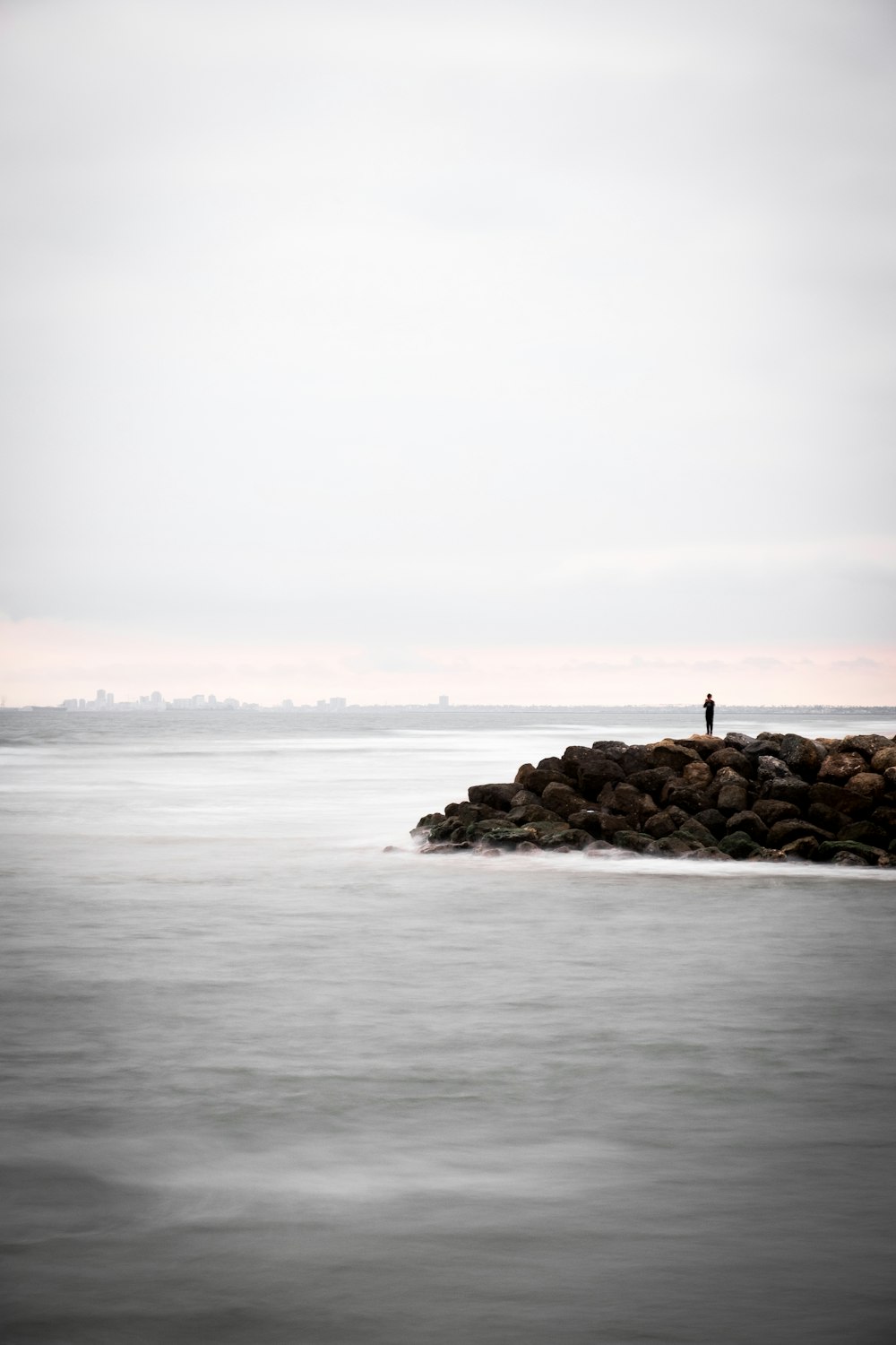 person standing on rocks surrounded by body of water