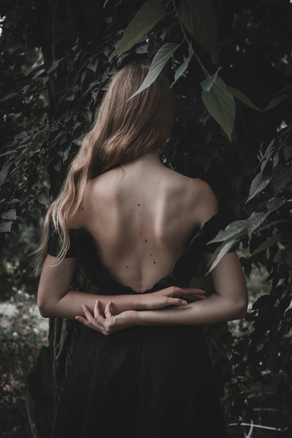 blonde woman with backless dress in forest surrounded by leaves