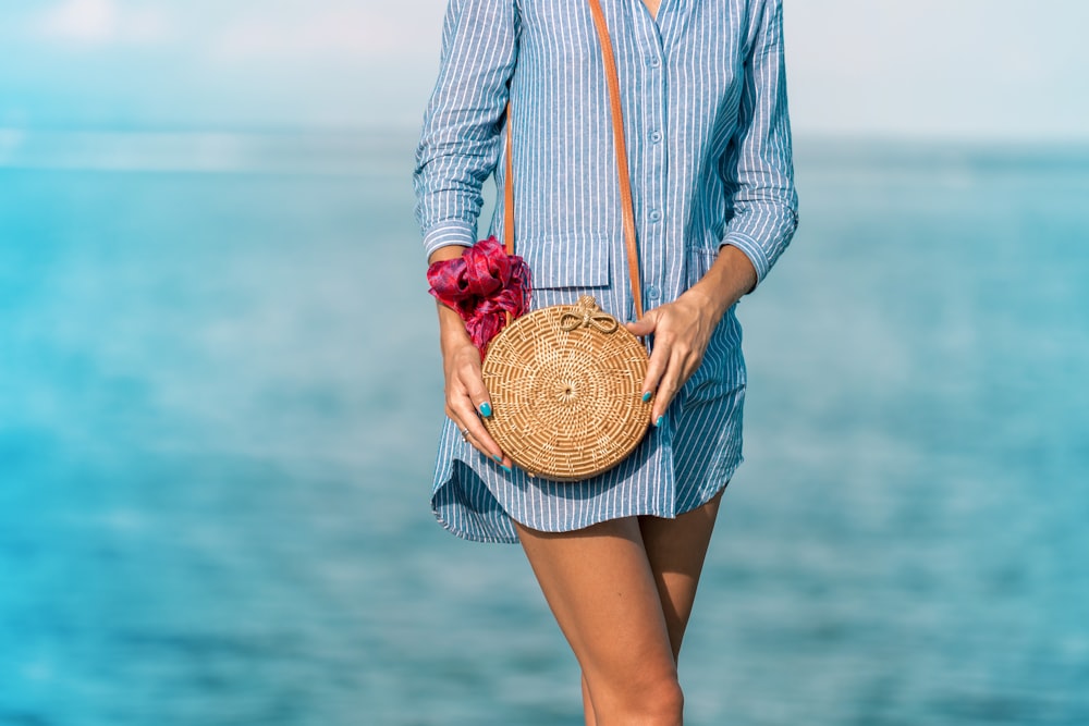 mulher vestindo azul e branco listrado vestido da camisa social com saco marrom do cruzamento do vime perto do mar durante o dia