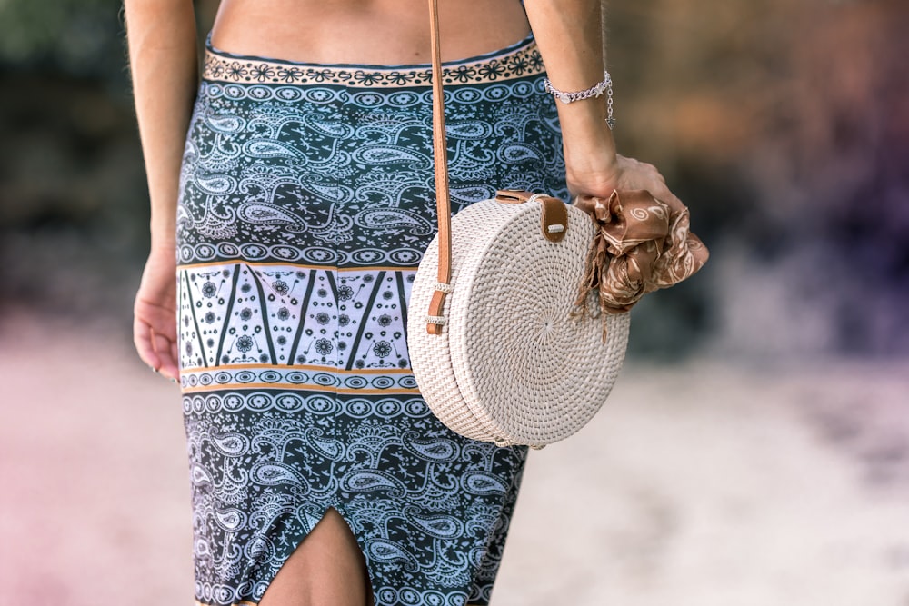 woman wearing blue paisley bottoms carrying white sling bag